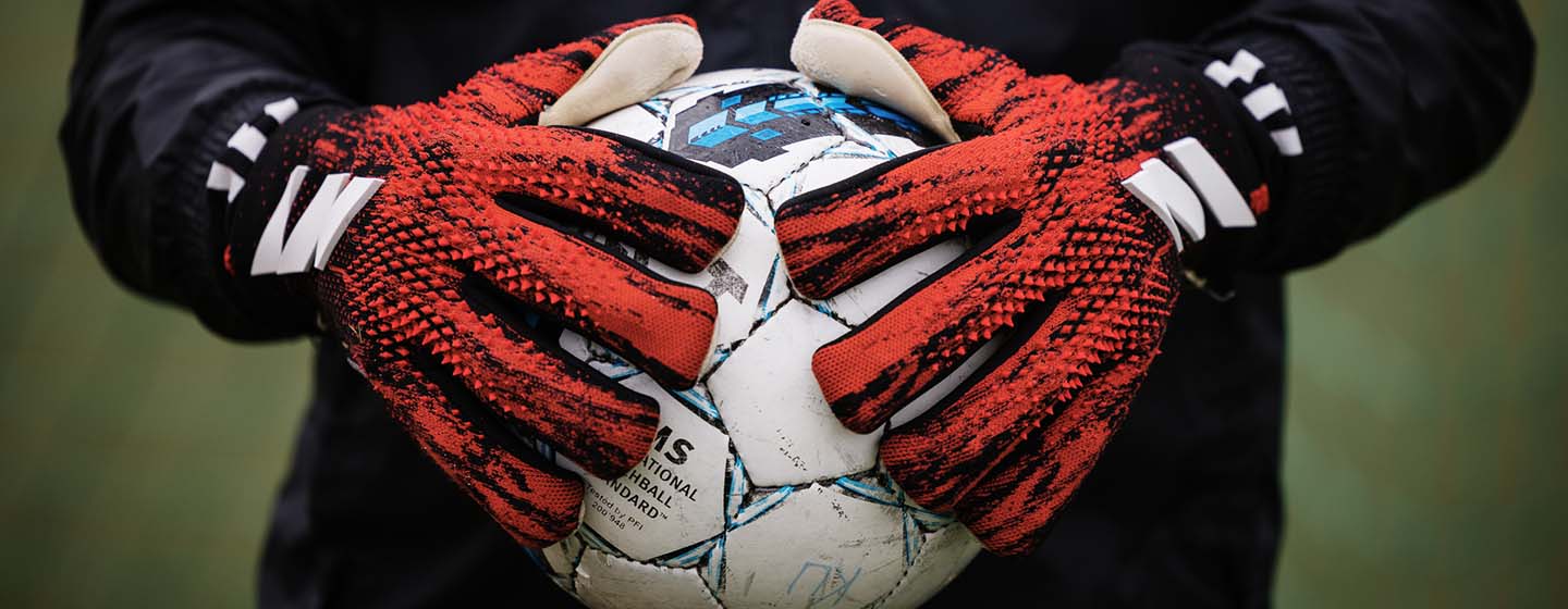 Fotbollsmålvakt med handskar som håller i en fotboll